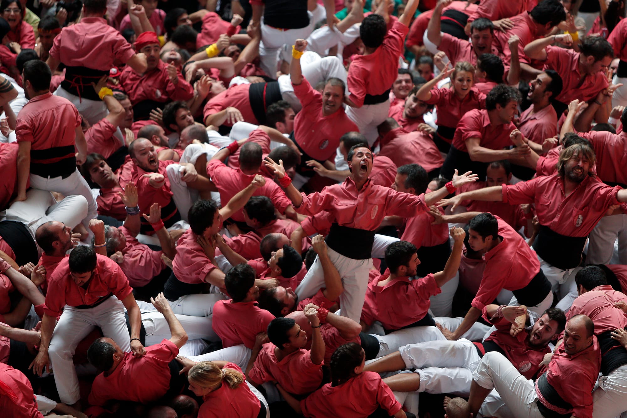 Castellers celebrando eufóricos con los brazos en alto, gritando de alegría en el centro de la plaza tras desmontar con éxito la torre humana.