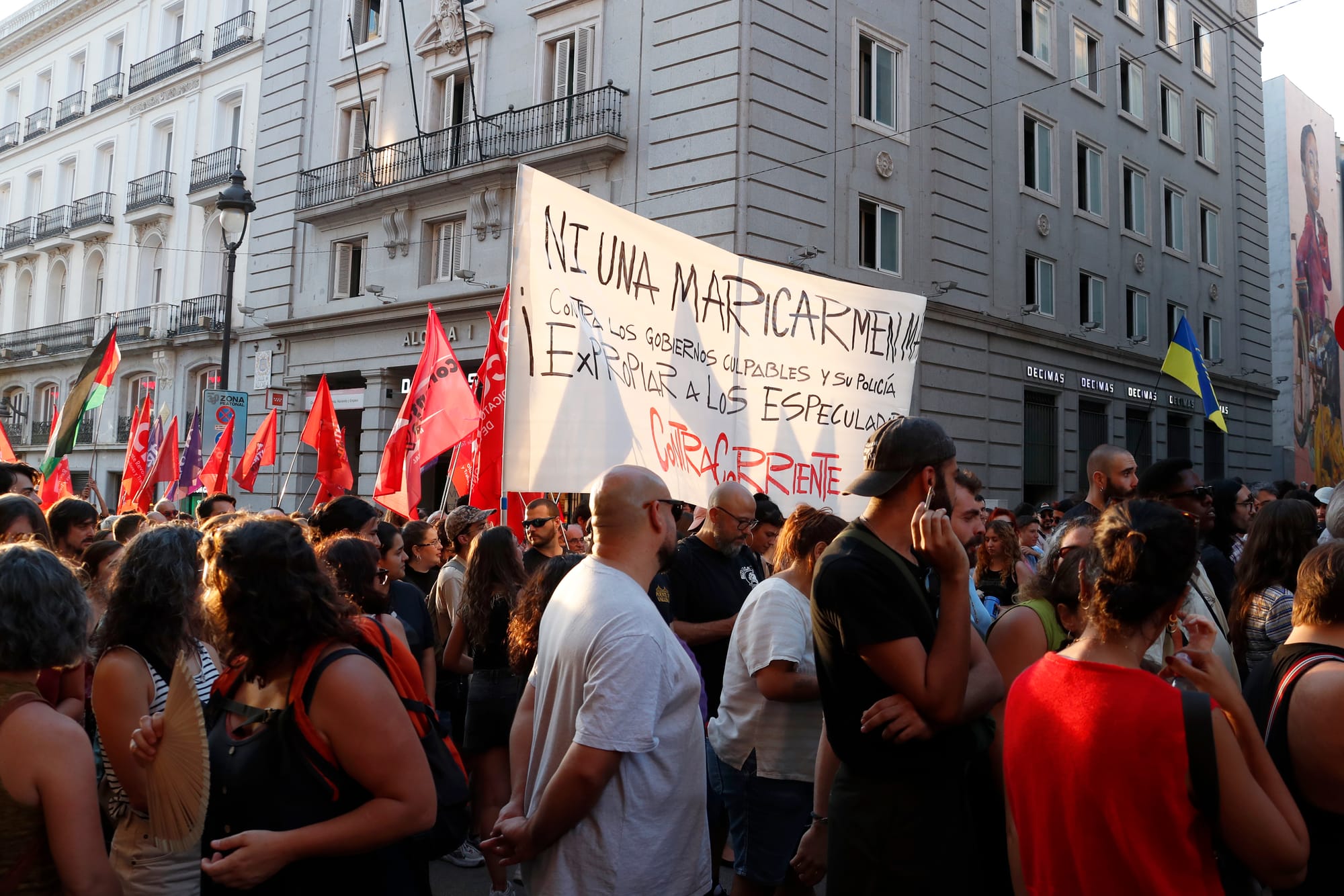 Multitud de manifestantes concentrados en una calle del centro de Madrid; en primer plano destaca una gran pancarta blanca con el texto 'NI UNA MARICARMEN MÁS' y 'EXPROPIAR A LOS ESPECULADORES' escrito en letras negras y rojas.