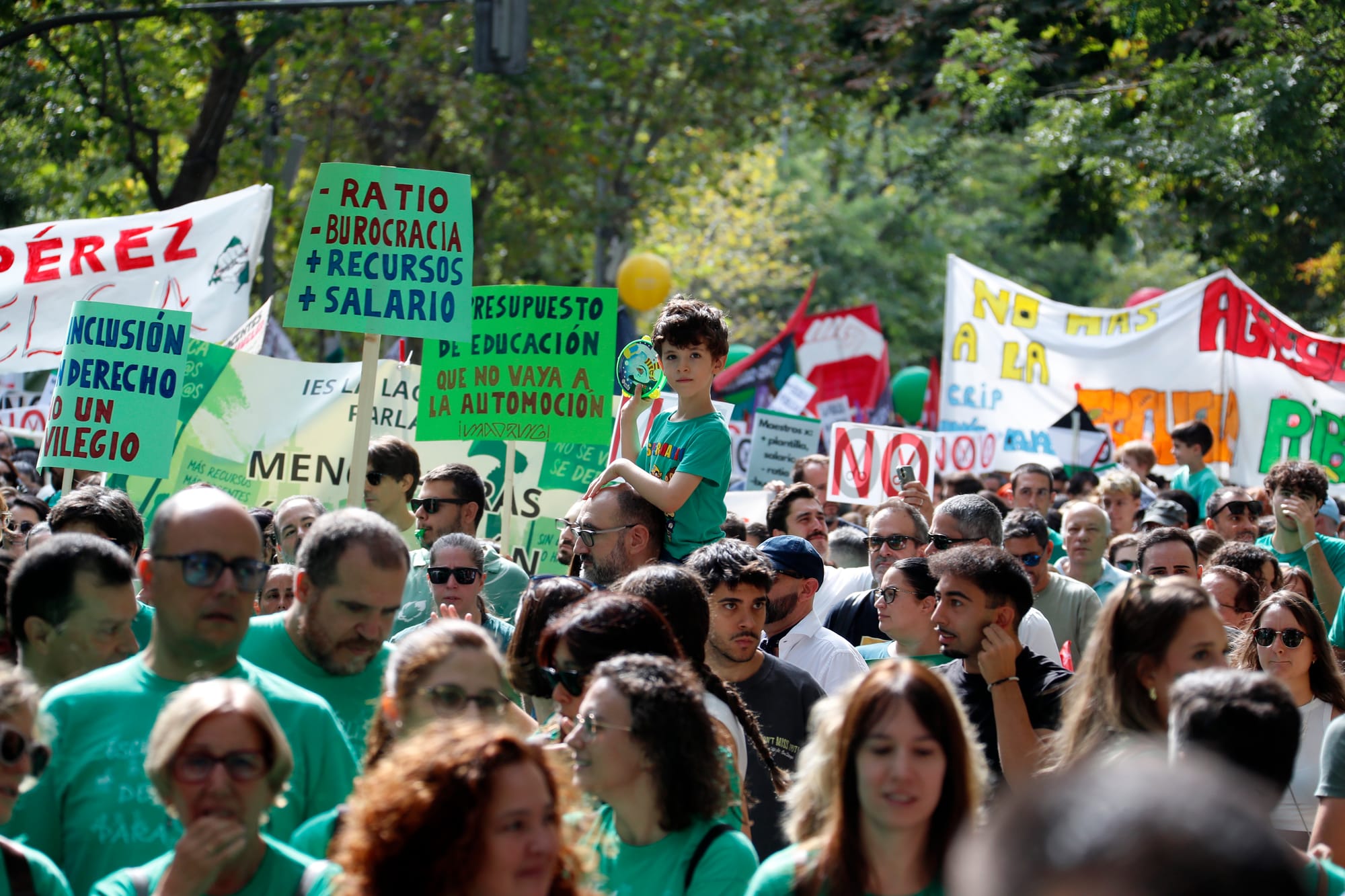Multitud de manifestantes con camisetas verdes marchando. En el centro destaca un niño subido a hombros junto a una pancarta verde con el texto '- RATIO, - BUROCRACIA, + RECURSOS, + SALARIO' y otra a la izquierda que indica 'LA INCLUSIÓN ES UN DERECHO NO UN PRIVILEGIO'.