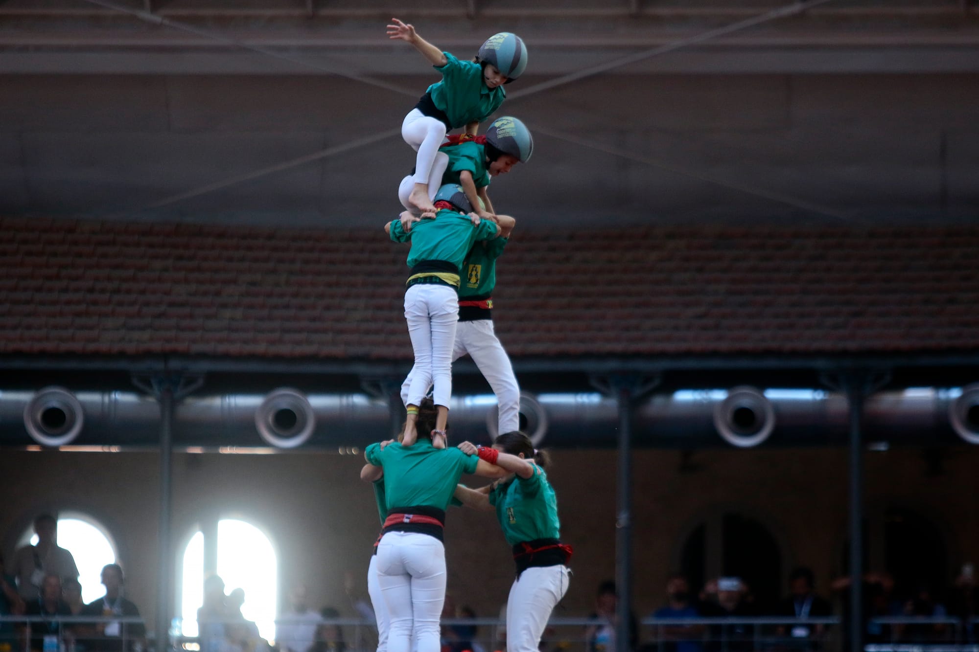 Una niña con casco protector en lo alto de una torre humana levanta un brazo al cielo para indicar que el castillo ha sido coronado con éxito.