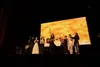 Escenario del Teatro Albéniz bajo la pantalla iluminada con el rótulo de Premios +Músicas, mostrando a Eva Amaral cantando con la guitarra rodeada por varias artistas invitadas.