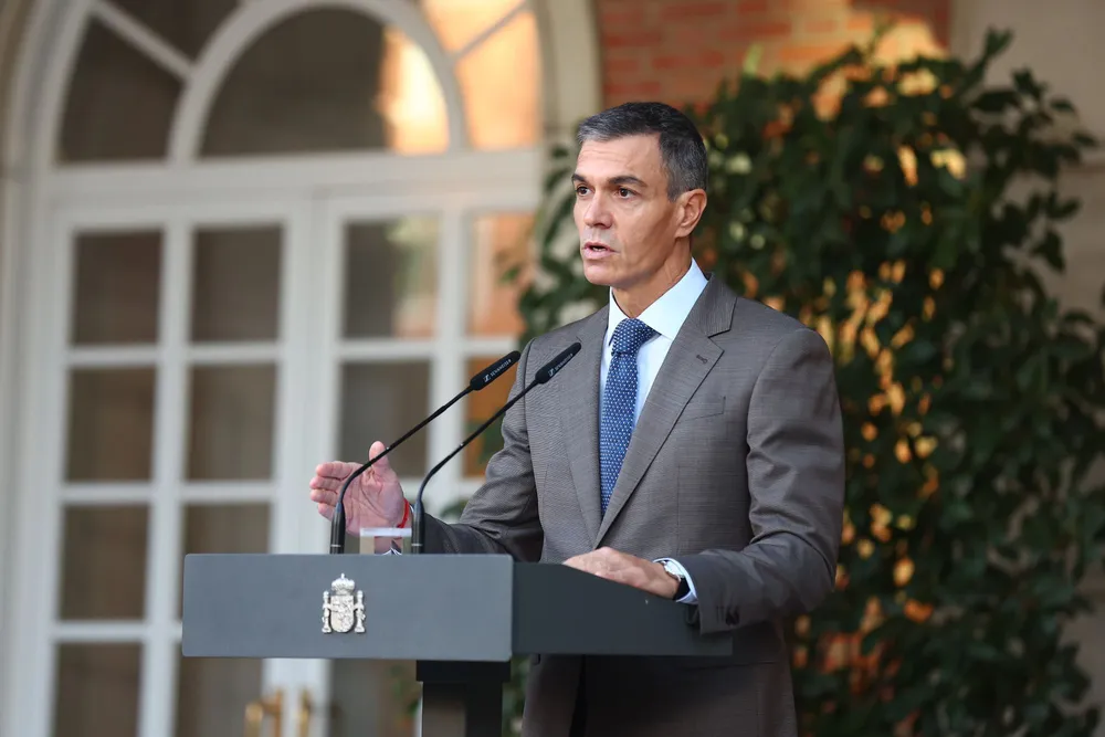 El presidente del Gobierno, Pedro Sánchez en el exterior del Palacio de la Moncloa, vistiendo traje gris y corbata azul, mientras habla desde el atril institucional.