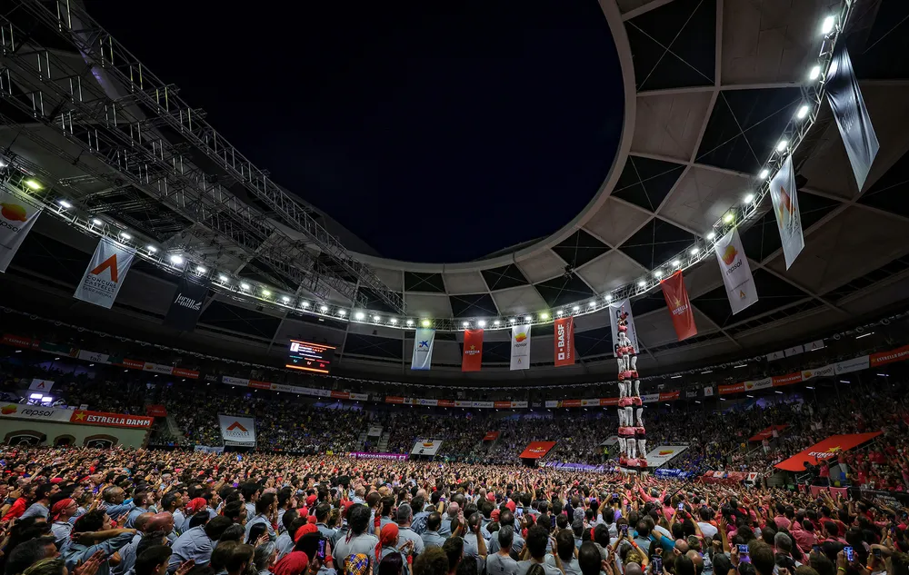 Interior de la Tarraco Arena Plaça donde la Colla Vella dels Xiquets de Valls levanta la estructura humana del 3 de 9 sense folre bajo la cúpula iluminada del recinto y ante una multitud.