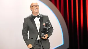 El actor Javier Cámara sonriendo frente a un micrófono, vistiendo esmoquin con un pin de apoyo a Palestina en la solapa, mientras sostiene el trofeo de la Concha de Plata del SSIFF.