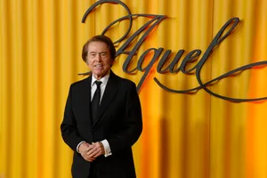 Fotografía de medio cuerpo del cantante Raphael posando sonriente con las manos cruzadas por delante. Viste un traje oscuro, camisa blanca y corbata negra.