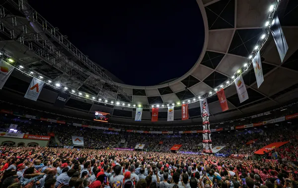 Interior de la Tarraco Arena Plaça donde la Colla Vella dels Xiquets de Valls levanta la estructura humana del 3 de 9 sense folre bajo la cúpula iluminada del recinto y ante una multitud.