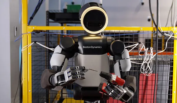 Fotografía en plano medio del robot humanoide Atlas en un laboratorio de pruebas, sujetando una punta de destornillador con la mano derecha y un taladro inalámbrico con la izquierda.